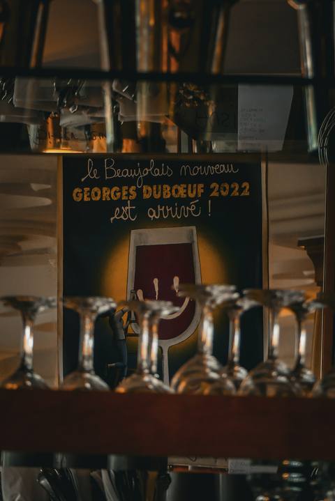 „Le Beaujolais nouveau est arrivé!“ – das Plakat hinter aufgereihten Gläsern im warmen Licht