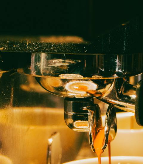 Espresso läuft aus dem Siebträger in die Tasse, alles im warmen Goldlicht